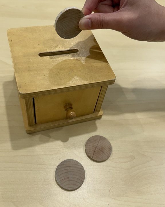 Hand posting a wooden disc through the slot of a wooden coin box