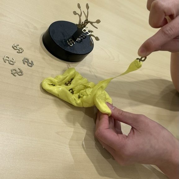 Fingers pulling a small hidden object out of yellow therapy putty in a dough treasure hunt